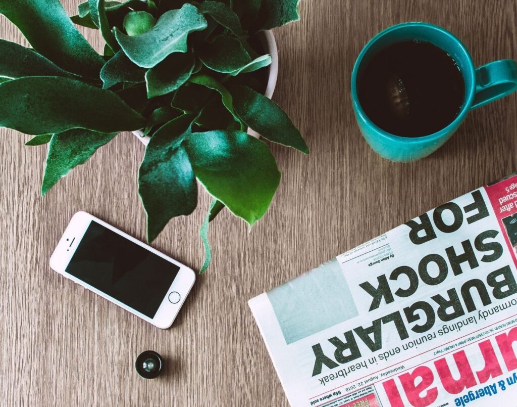 Zeitung, Handy, Pflanze und eine Tasse Kaffee auf einemTisch